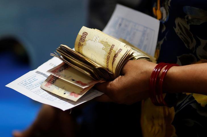 A woman holds 500 and 1000 Indian rupee banknotes as she stands in a queue to deposit her money inside a bank in the northern city of Kanpur